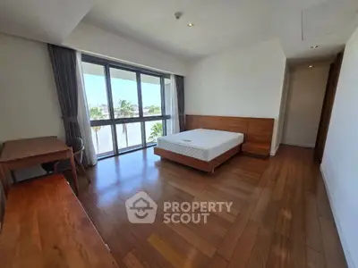 Spacious bedroom with wooden flooring and large windows offering natural light.