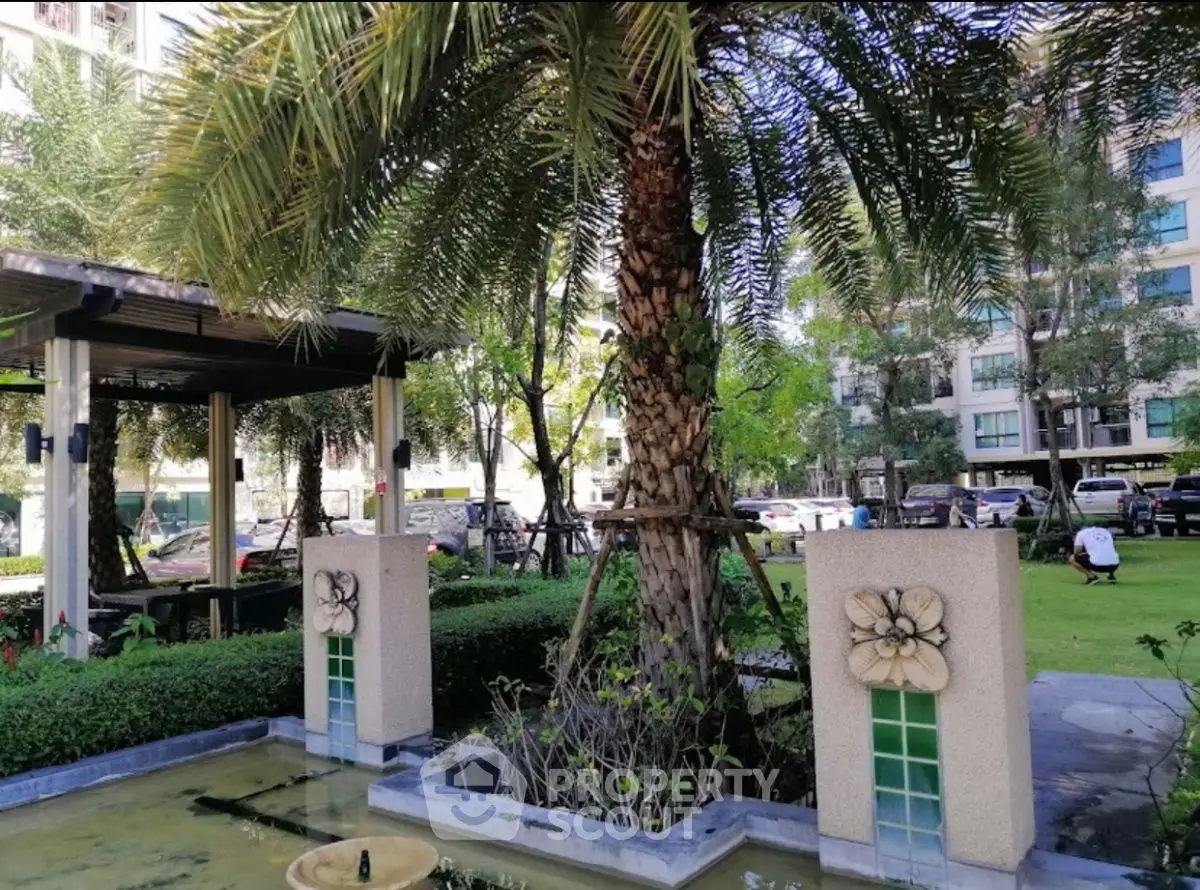 Lush garden area with palm tree and decorative water feature in modern residential complex.