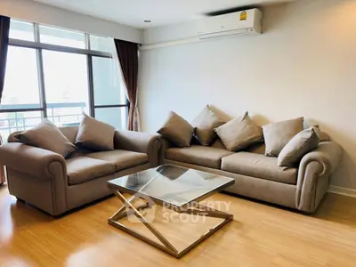 Spacious living room with modern sofas and glass coffee table, featuring large windows for natural light.