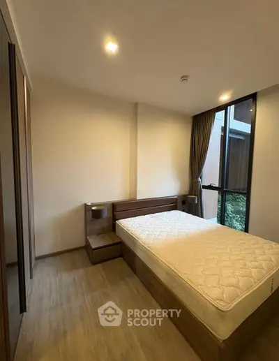 Modern bedroom with large window and wooden flooring in a stylish apartment.