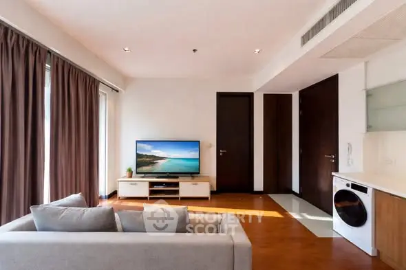 Modern living room with sleek furniture and natural light, featuring a flat-screen TV and stylish decor.