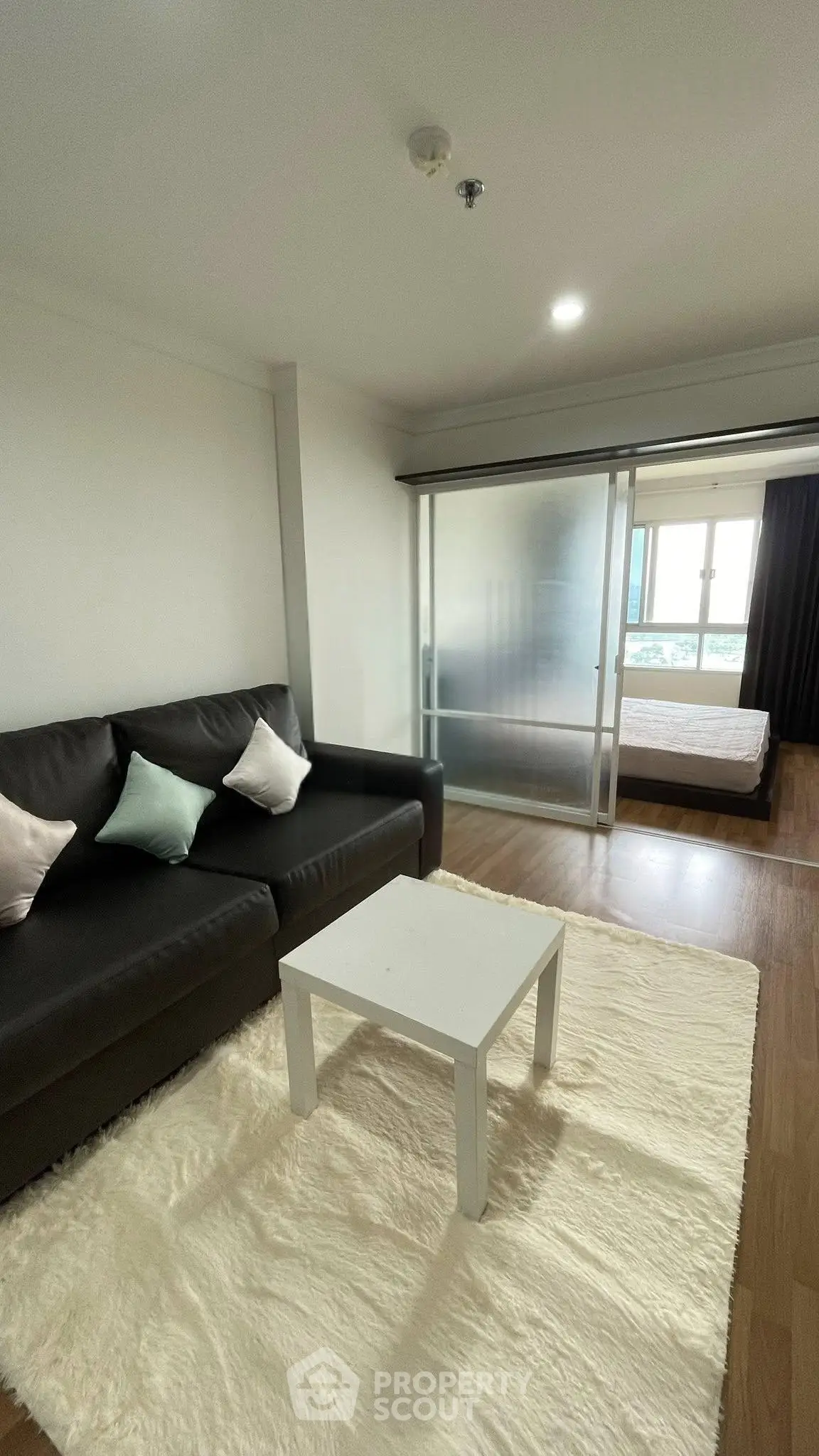 Modern living room with cozy sofa and sliding glass doors leading to a bright bedroom.