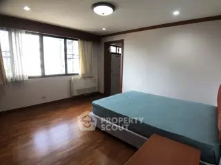 Spacious bedroom with large window and wooden flooring in modern apartment.