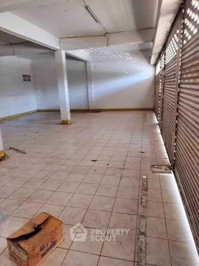 Spacious empty commercial space with tiled flooring and shuttered windows, ideal for business setup.