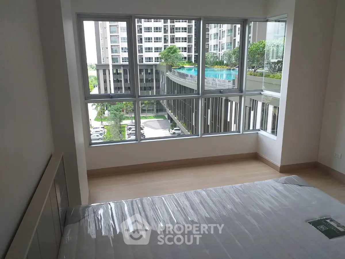 Spacious bedroom with large windows offering a stunning view of the pool and modern building exterior.