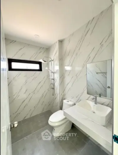 Modern bathroom with sleek design and marble walls, featuring a stylish sink and shower area.