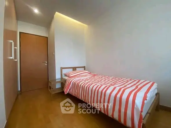 Cozy minimalist bedroom with wooden flooring and striped bedding in modern apartment.