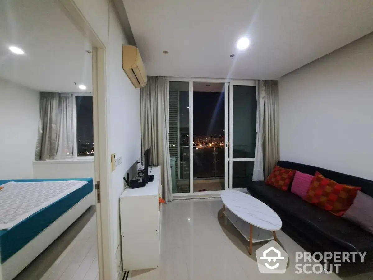 Modern studio apartment with a seamless blend of bedroom and living space, featuring a comfortable bed, stylish sofa, and a captivating city view through the large glass door leading to the balcony.