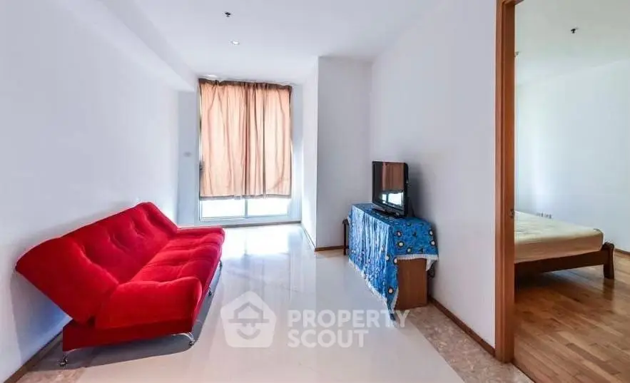 Bright living room with red sofa and adjacent bedroom in modern apartment