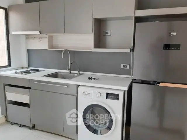 Modern kitchen with sleek cabinets, washing machine, and stainless steel fridge.