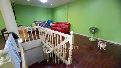 Spacious living room with vibrant green walls and wooden flooring, featuring a red sofa and staircase.