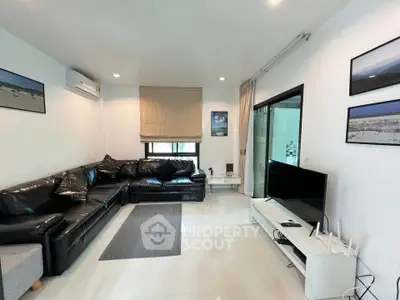 Spacious modern living room with sleek black leather sofas and a flat-screen TV, perfect for relaxation.