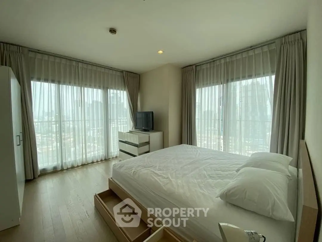 Spacious bedroom with large windows and city view, featuring modern furniture and ample natural light.