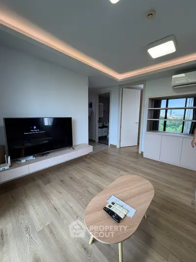 Modern living room with wooden flooring, sleek TV setup, and natural light from large windows.