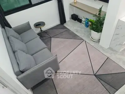 Modern living room with stylish gray sofa and geometric rug, featuring a sleek side table and lush green plant.