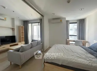 Modern studio apartment with open layout, featuring a cozy bed, stylish sofa, and a balcony with city views.