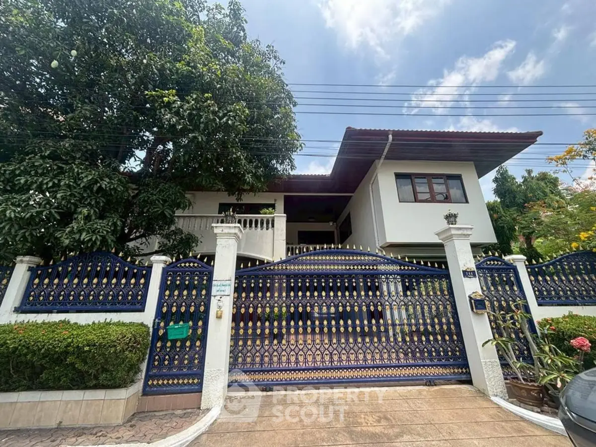 Charming two-story house with ornate gate and lush greenery, perfect for family living.