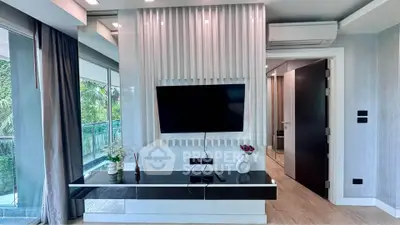 Modern living room with sleek TV setup and large windows offering lush greenery views.
