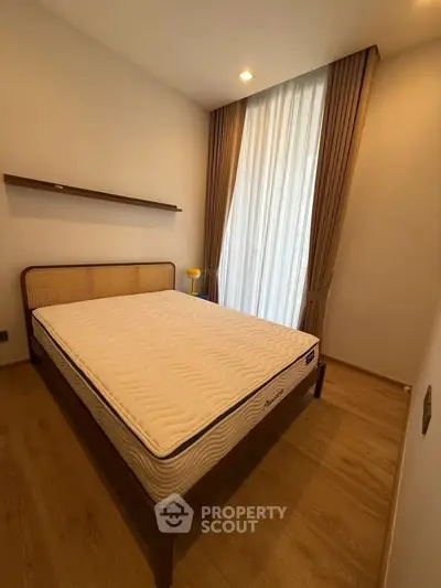 Cozy bedroom with wooden flooring and natural light from large window, perfect for relaxation.