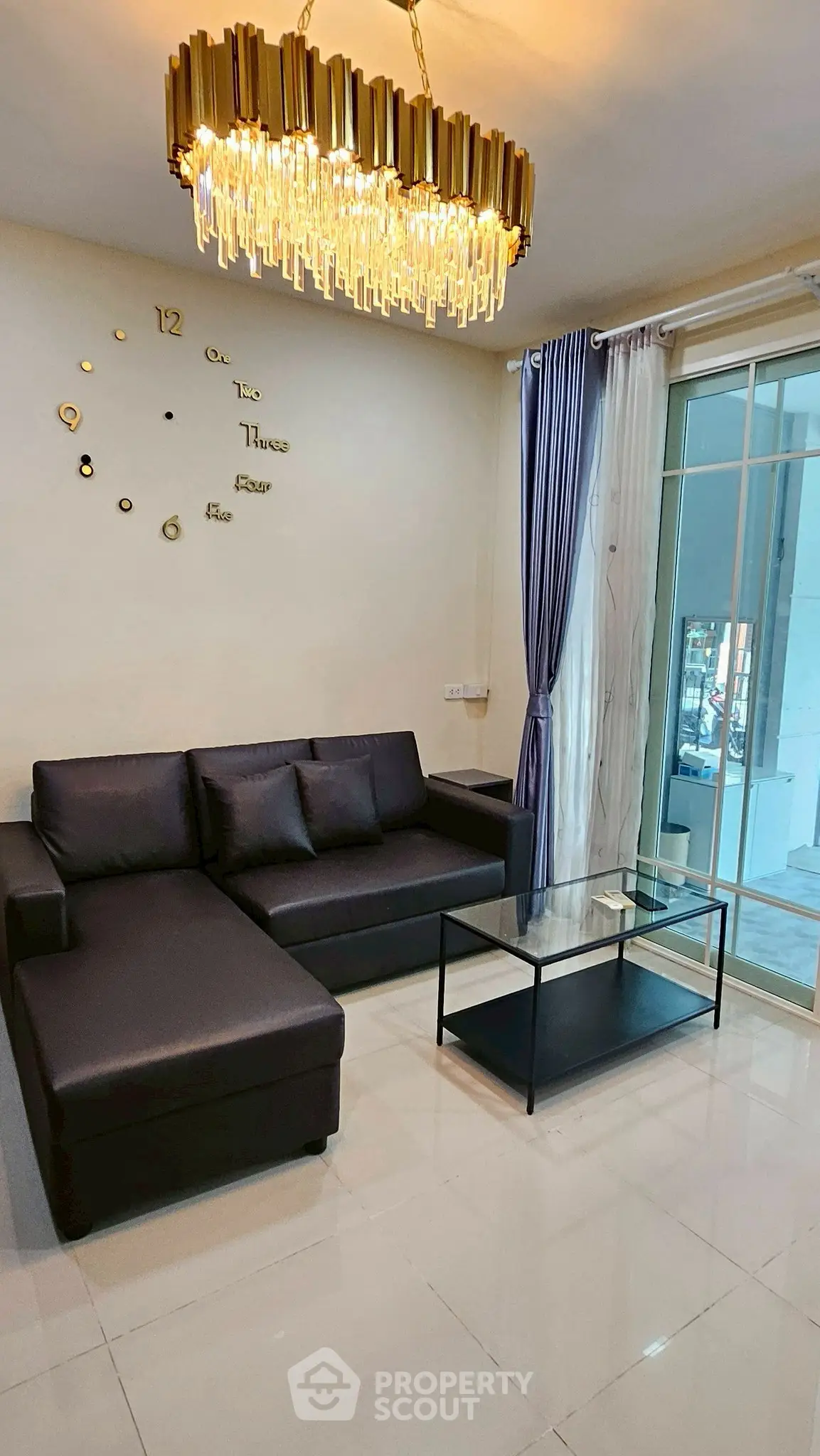 Modern living room with sleek black sofa, glass coffee table, and elegant chandelier.