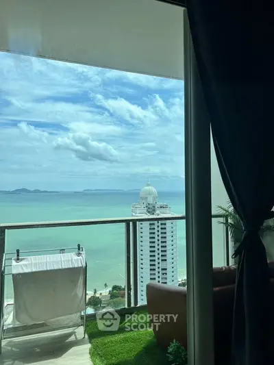 Stunning ocean view from a high-rise balcony with lush green artificial grass and cozy seating area.
