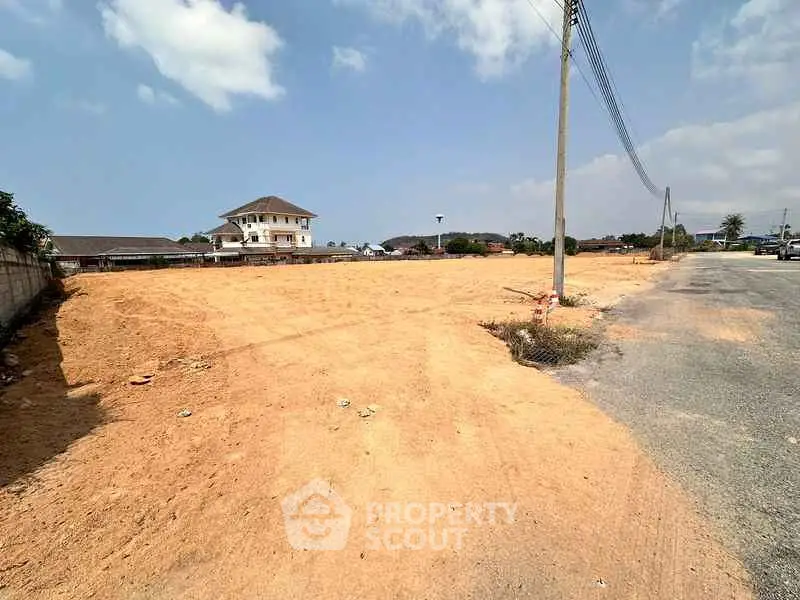 Expansive vacant land with potential for development, featuring clear skies and a distant view of a residential building.