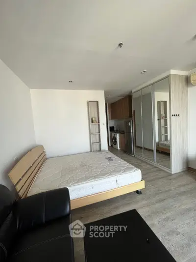 Modern studio apartment with sleek design, featuring a cozy bed, mirrored wardrobe, and compact kitchen area.
