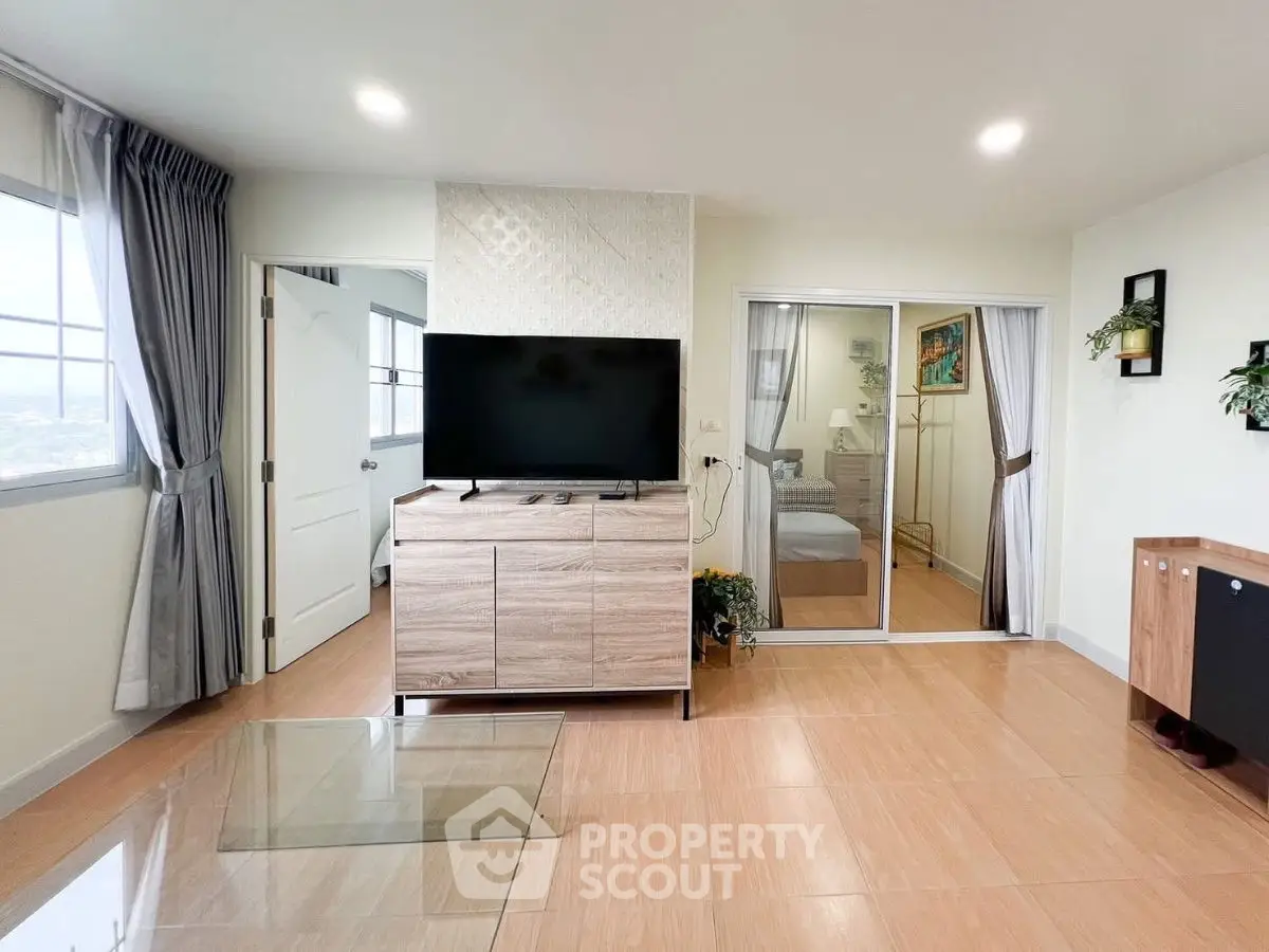 Modern living room with TV, glass table, and view into bedroom