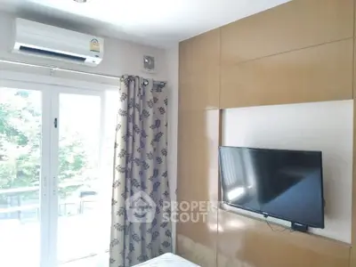 Modern bedroom with wall-mounted TV and air conditioning, featuring large windows with leafy view.