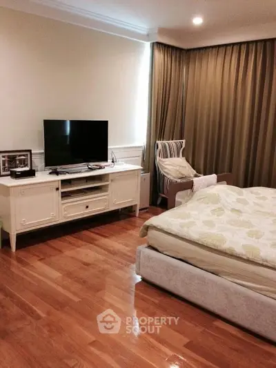 Cozy bedroom with wooden flooring, elegant curtains, and a modern TV setup.