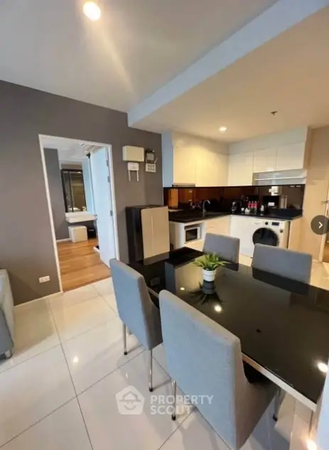 Modern kitchen and dining area with sleek black table and gray chairs in a stylish apartment.