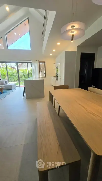 Spacious modern dining area with high ceilings and natural light, featuring a wooden table and garden view.