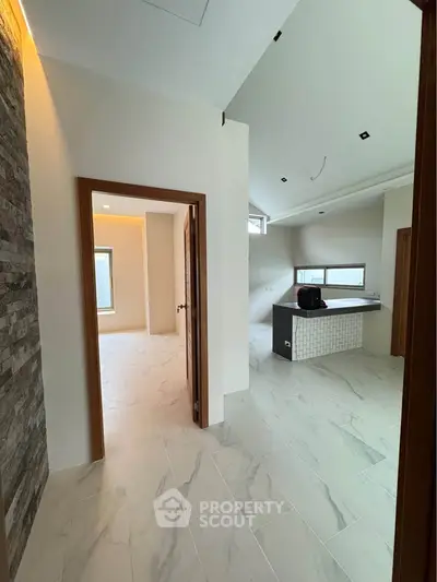 Modern open-layout interior with sleek kitchen and stone accent wall, featuring large windows for natural light.