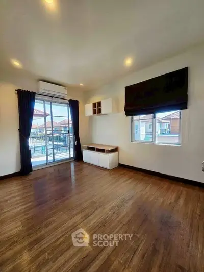 Spacious living room with wooden flooring and large windows offering natural light and balcony access.