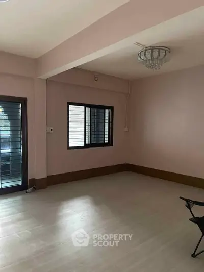 Spacious empty room with modern chandelier and large window, perfect for customization.