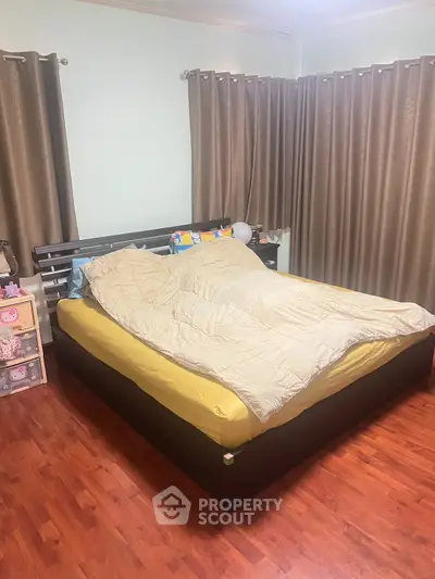 Cozy bedroom with wooden flooring and elegant curtains, featuring a comfortable bed and ample natural light.