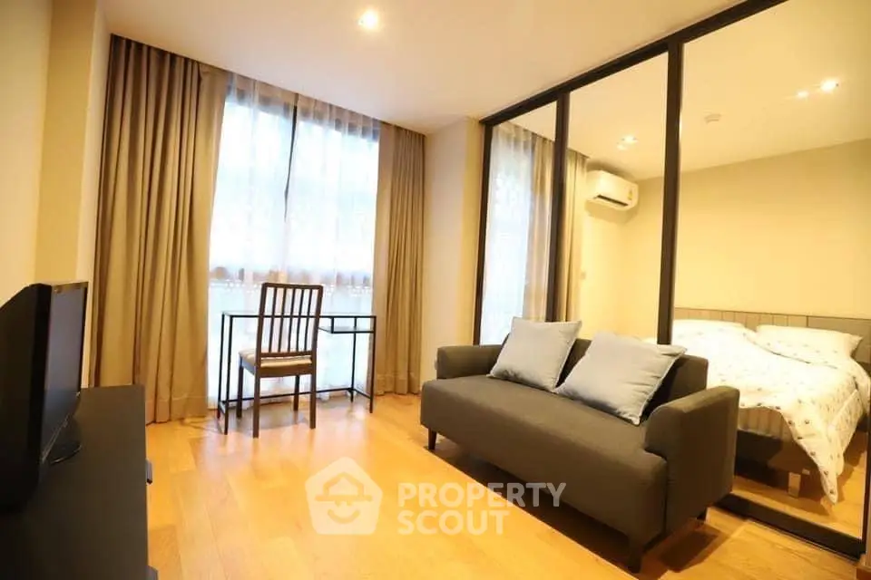 Cozy bedroom with sofa and large window, featuring wooden flooring and modern decor.