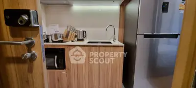 Modern compact kitchen with wooden cabinets, stainless steel fridge, and sleek appliances.