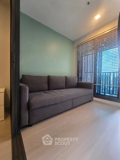 Modern living room with sleek sofa and large window offering city view.