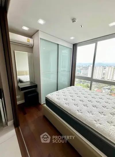 Modern bedroom with large window offering stunning city views, featuring a comfortable bed and sleek wooden flooring.