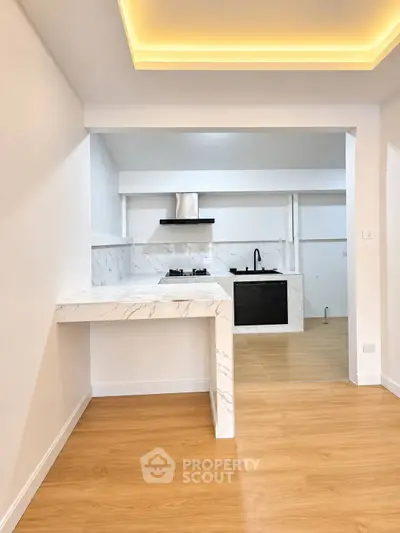 Modern kitchen with marble countertops and open layout, featuring sleek appliances and warm wooden flooring.