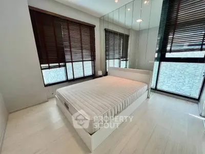 Modern bedroom with large windows and mirrored wall, featuring sleek design and natural light.
