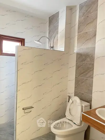 Modern bathroom with tiled walls and shower area, featuring a toilet and sink.