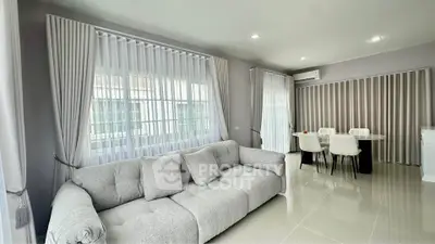 Spacious modern living room with elegant sofa and dining area, featuring large windows and sleek tile flooring.