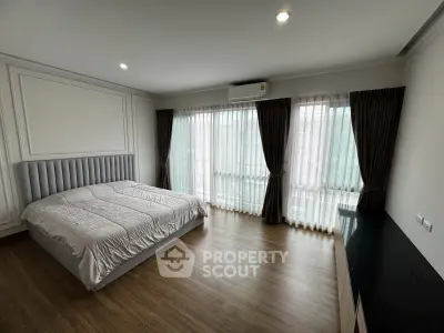 Spacious bedroom with large windows and modern decor, featuring elegant curtains and wooden flooring.
