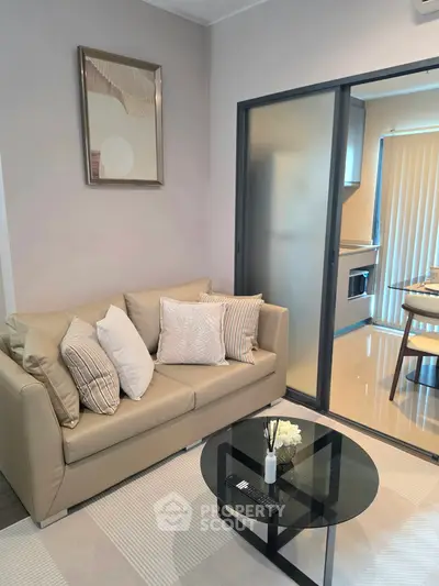 Modern living room with beige sofa, glass coffee table, and sliding door to kitchen.