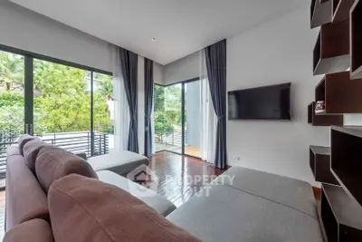 Modern living room with large windows and stylish furniture overlooking lush greenery.