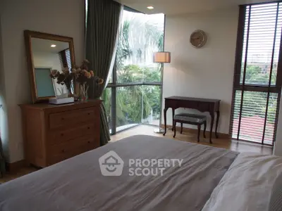 Spacious bedroom with large windows and elegant decor, offering a serene view of lush greenery.