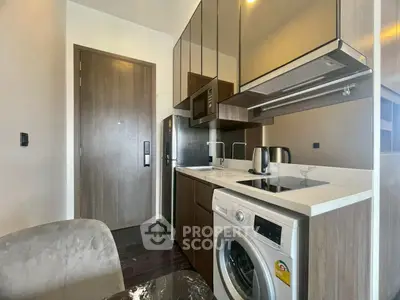 Modern compact kitchen with washing machine and sleek cabinetry in a stylish apartment.