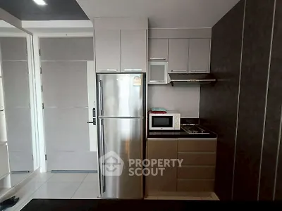 Modern compact kitchen with stainless steel fridge and microwave in sleek apartment.